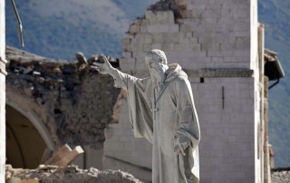 A staue before a church crumbled by earthquakes